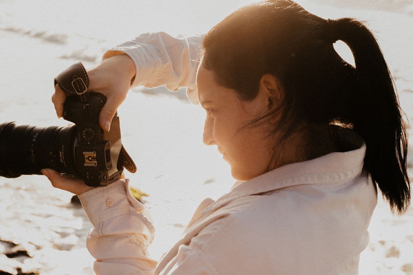 Une photographe en chemise claire ajuste son appareil dans une lumière naturelle